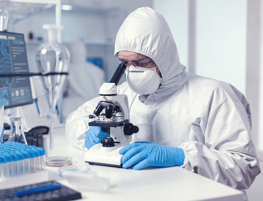 Scientist in protective gear looking through a microscope